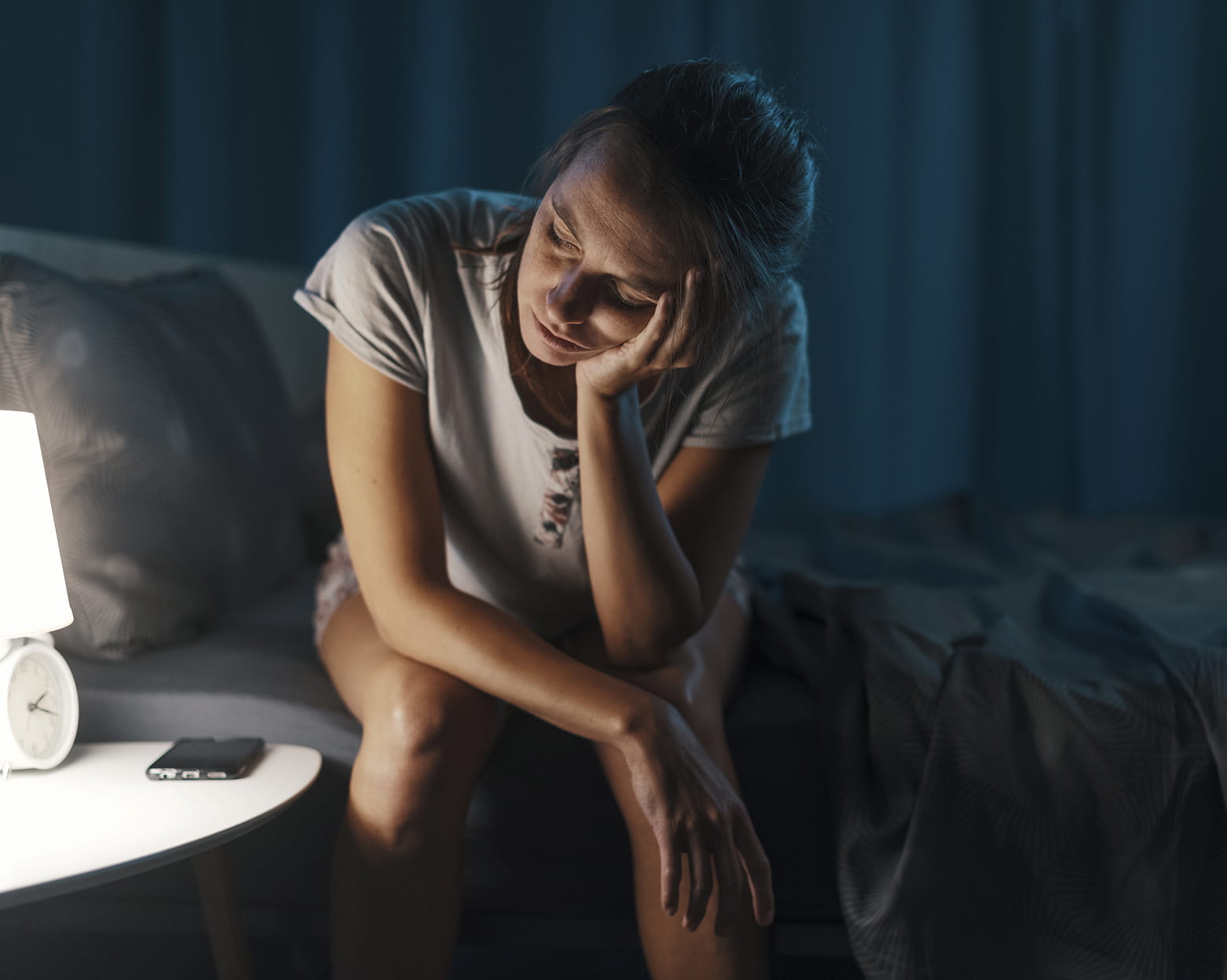 Woman sitting on bed struggling to sleep.